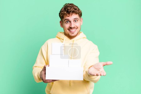Téléchargez les photos : Young adult caucasian man smiling happily with friendly and  offering and showing a concept. blank different packages concept - en image libre de droit