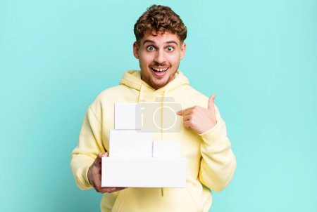 Téléchargez les photos : Young adult caucasian man feeling happy and pointing to self with an excited. blank different packages concept - en image libre de droit