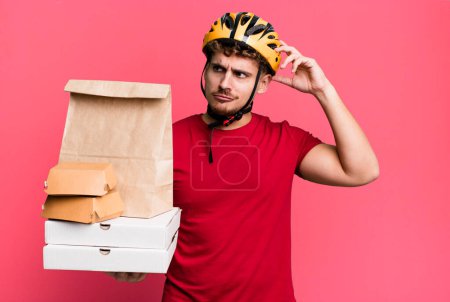 Photo for Young adult caucasian man feeling puzzled and confused, scratching head.  take away fast food deliveryman concept - Royalty Free Image