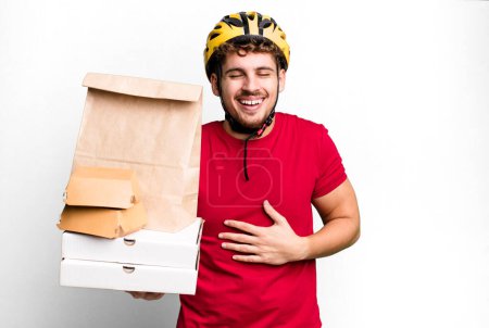 Téléchargez les photos : Young adult caucasian man laughing out loud at some hilarious joke.  take away fast food deliveryman concept - en image libre de droit