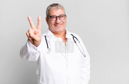 Téléchargez les photos : Homme âgé d'âge moyen souriant et l'air amical, montrant le numéro deux. concept médecin ou médecin - en image libre de droit