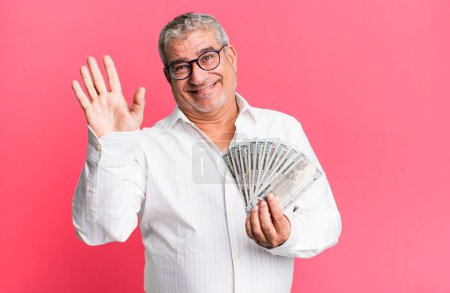 Photo for Middle age senior man smiling happily, waving hand, welcoming and greeting you. dollar banknotes concept - Royalty Free Image