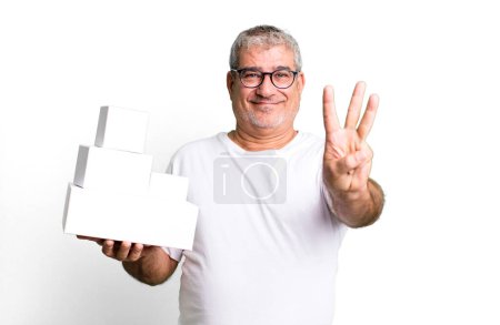 Téléchargez les photos : Homme âgé d'âge moyen souriant et l'air amical, montrant le numéro trois. différents paquets boîtes vides - en image libre de droit