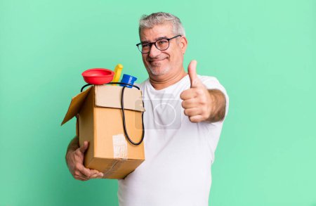 Foto de Hombre mayor de mediana edad sintiéndose orgulloso, sonriendo positivamente con los pulgares hacia arriba. ama de llaves reparador con un concepto de caja de herramientas - Imagen libre de derechos