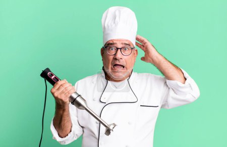 Foto de Hombre mayor de mediana edad sintiéndose estresado, ansioso o asustado, con las manos en la cabeza. chef de restaurante con un concepto de herramienta - Imagen libre de derechos
