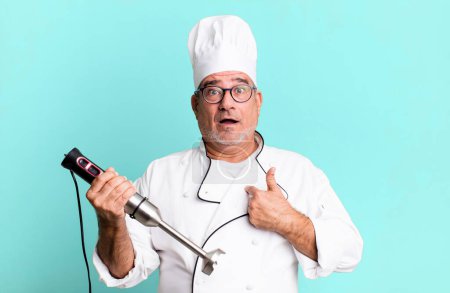 Photo for Middle age senior man looking shocked and surprised with mouth wide open, pointing to self. restaurant chef with a tool concept - Royalty Free Image