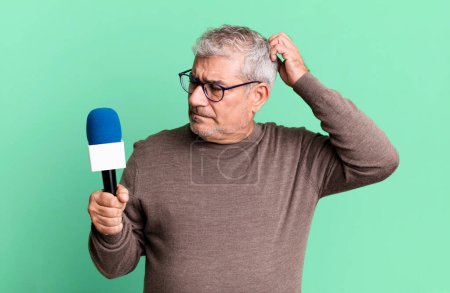 Téléchargez les photos : Homme âgé d'âge moyen se sentant perplexe et confus, tête grattée. journaliste ou présentateur de télévision avec un micro - en image libre de droit