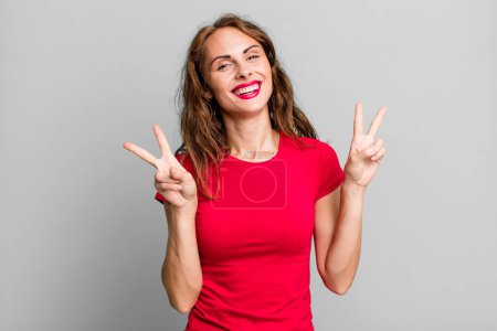 Photo for Young pretty woman smiling and looking happy, friendly and satisfied, gesturing victory or peace with both hands - Royalty Free Image