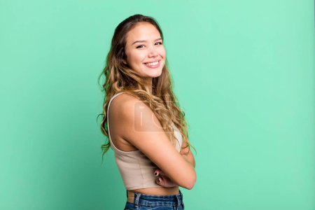 Photo for Young pretty woman smiling to camera with crossed arms and a happy, confident, satisfied expression, lateral view - Royalty Free Image