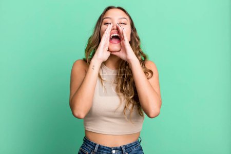 Photo for Young pretty woman feeling happy, excited and positive, giving a big shout out with hands next to mouth, calling out - Royalty Free Image