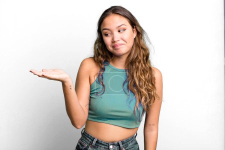 Photo for Young pretty woman feeling happy and smiling casually, looking to an object or concept held on the hand on the side - Royalty Free Image