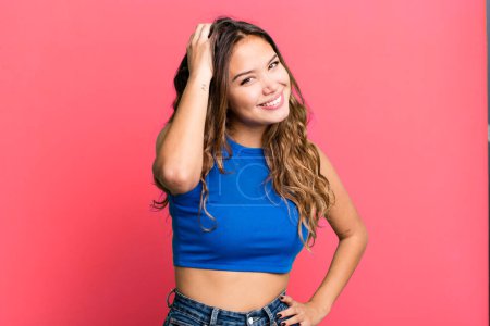 Photo for Young pretty woman smiling cheerfully and casually, taking hand to head with a positive, happy and confident look - Royalty Free Image