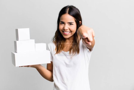 Photo for Hispanic pretty woman pointing at camera choosing you with blank packages boxes - Royalty Free Image