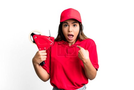 Photo for Hispanic pretty woman looking shocked and surprised with mouth wide open, pointing to self. packer and delivery employee - Royalty Free Image