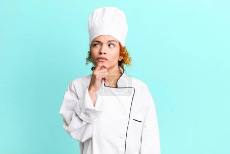Foto de Cabello rojo bonita mujer pensando, sintiéndose dudoso y confundido. concepto de chef - Imagen libre de derechos
