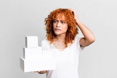 Foto de Red hair pretty woman smiling happily and daydreaming or doubting. blank packages boxes concept - Imagen libre de derechos