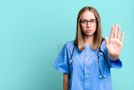 Téléchargez les photos : Regardant sérieux montrant la paume ouverte faisant geste d'arrêt. concept d'infirmière - en image libre de droit