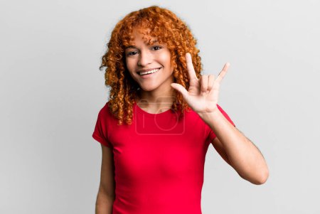 Photo for Redhair pretty woman feeling happy, fun, confident, positive and rebellious, making rock or heavy metal sign with hand - Royalty Free Image