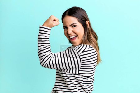 Photo for Hispanic pretty woman feeling happy, satisfied and powerful, flexing fit and muscular biceps, looking strong after the gym - Royalty Free Image