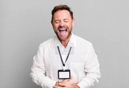 Téléchargez les photos : Homme d'âge moyen riant à haute voix à une blague hilarante. vip pass id accréditation - en image libre de droit
