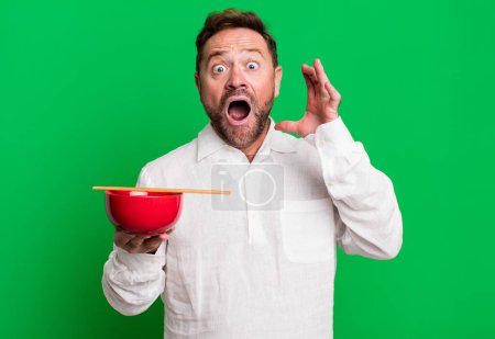 Photo for Middle age man screaming with hands up in the air. breakfast bowl - Royalty Free Image