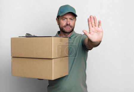 middle age man looking serious showing open palm making stop gesture. paker delivery man. packer delivery man