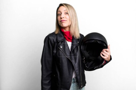 Foto de Pretty blonde woman shrugging, feeling confused and uncertain. motorbike rider and helmet concept - Imagen libre de derechos