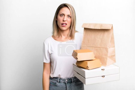 Téléchargez les photos : Pretty blonde woman feeling puzzled and confused. paper fast food take away packages - en image libre de droit