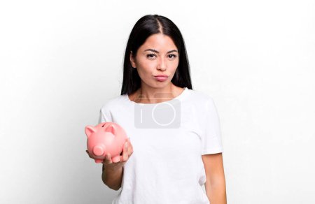 Photo for Hispanic pretty woman feeling sad and whiney with an unhappy look and crying with a piggy bank - Royalty Free Image