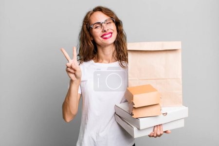 Foto de Hispanic pretty woman smiling and looking friendly, showing number two. take away fast food packages concept - Imagen libre de derechos