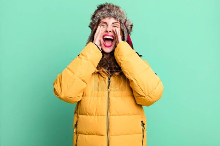 Foto de Hispanic pretty woman feeling happy,giving a big shout out with hands next to mouth. wearing an anorak. cold and winter concept - Imagen libre de derechos