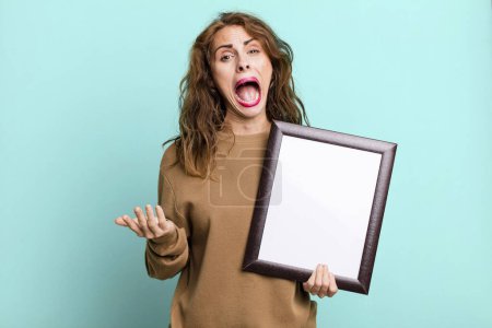 Photo for Hispanic pretty woman looking desperate, frustrated and stressed with an empty blank frame - Royalty Free Image