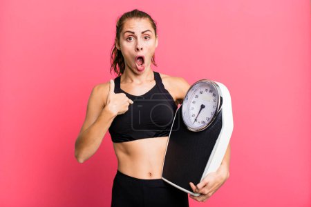 Téléchargez les photos : Hispanic pretty woman looking shocked and surprised with mouth wide open, pointing to self. fitness, diet and weight scale concept - en image libre de droit