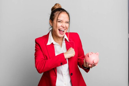 Photo for Hispanic pretty woman feeling happy and facing a challenge or celebrating with a piggy bank - Royalty Free Image