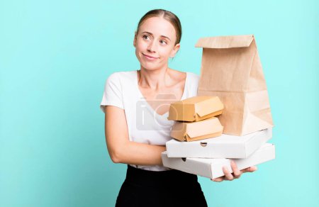Foto de Caucasian pretty woman shrugging, feeling confused and uncertain. with fast food packages. delivery concept - Imagen libre de derechos