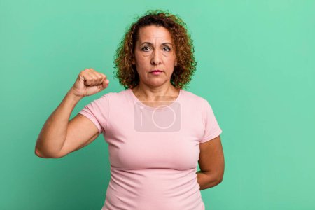 Photo for Middle age hispanic woman feeling serious, strong and rebellious, raising fist up, protesting or fighting for revolution - Royalty Free Image