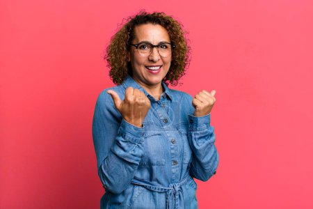 Photo for Middle age hispanic woman smiling joyfully and looking happy, feeling carefree and positive with both thumbs up - Royalty Free Image