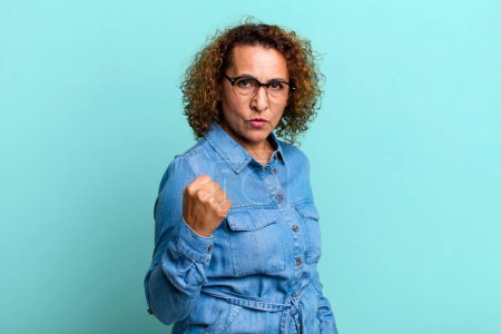 Téléchargez les photos : Femme hispanique d'âge moyen se sentant en colère, agacé, rebelle et agressif, retournant le majeur, se battant en arrière - en image libre de droit