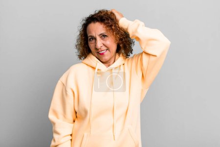 Photo for Middle age hispanic woman smiling cheerfully and casually, taking hand to head with a positive, happy and confident look - Royalty Free Image