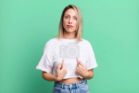 Foto de Blonde adult woman pointing to self with a confused and quizzical look, shocked and surprised to be chosen - Imagen libre de derechos