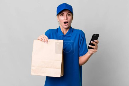Photo for Pretty caucasian  delivery woman with a paper bag and a phone - Royalty Free Image