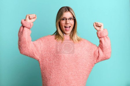 Foto de Rubia bonita mujer gritando triunfalmente, pareciendo emocionada, feliz y sorprendida ganadora, celebrando - Imagen libre de derechos