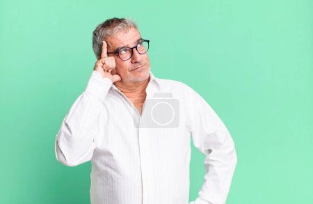 Foto de Hombre mayor de mediana edad con una mirada concentrada, preguntándose con una expresión dudosa, mirando hacia arriba y hacia un lado - Imagen libre de derechos