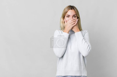 Foto de Caucasian blonde woman covering mouth with hands with a shocked. copy space concept - Imagen libre de derechos