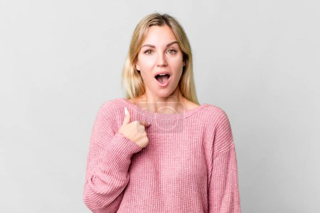 Photo for Caucasian blonde woman looking shocked and surprised with mouth wide open, pointing to self - Royalty Free Image