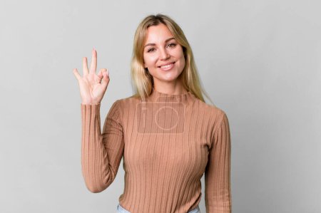 Foto de Caucasian blonde woman feeling happy, showing approval with okay gesture - Imagen libre de derechos