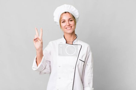 Foto de Caucasian blonde woman smiling and looking friendly, showing number two. chef concept - Imagen libre de derechos
