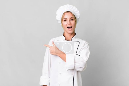 Foto de Caucasian blonde woman looking excited and surprised pointing to the side. chef concept - Imagen libre de derechos