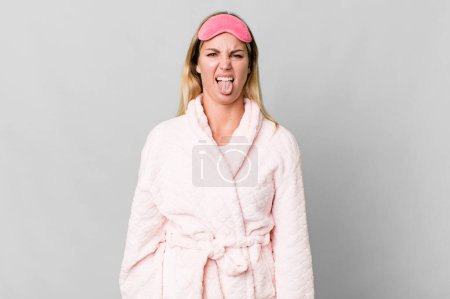 Foto de Caucasian blonde woman feeling disgusted and irritated and tongue out. night wear concept - Imagen libre de derechos