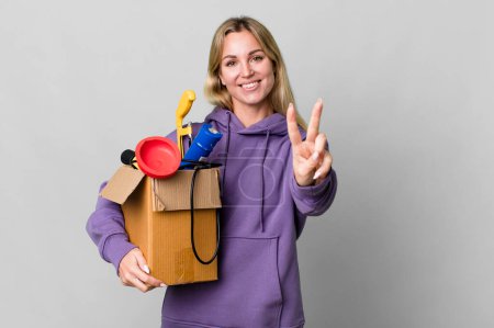 Photo for Caucasian blonde woman smiling and looking happy, gesturing victory or peace. housekeeper concept - Royalty Free Image